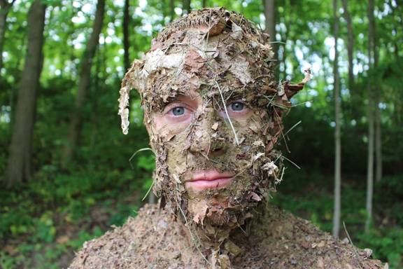 Visage d'un homme recouvert de débris forestiers pour un camouflage naturel.
