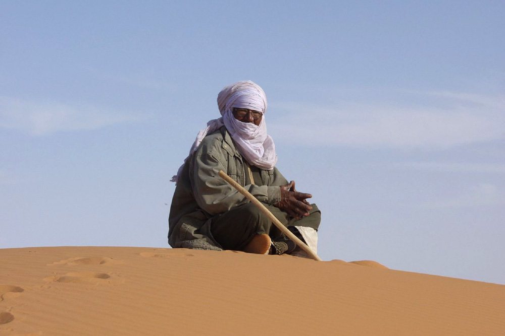 Homme assis au sommet d'une dune de sable.
