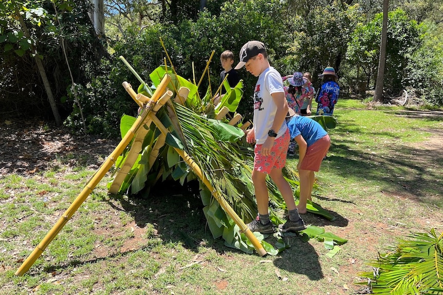 Les enfants construisent un abri de survie à partir de feuilles de palmier vertes et de branches.