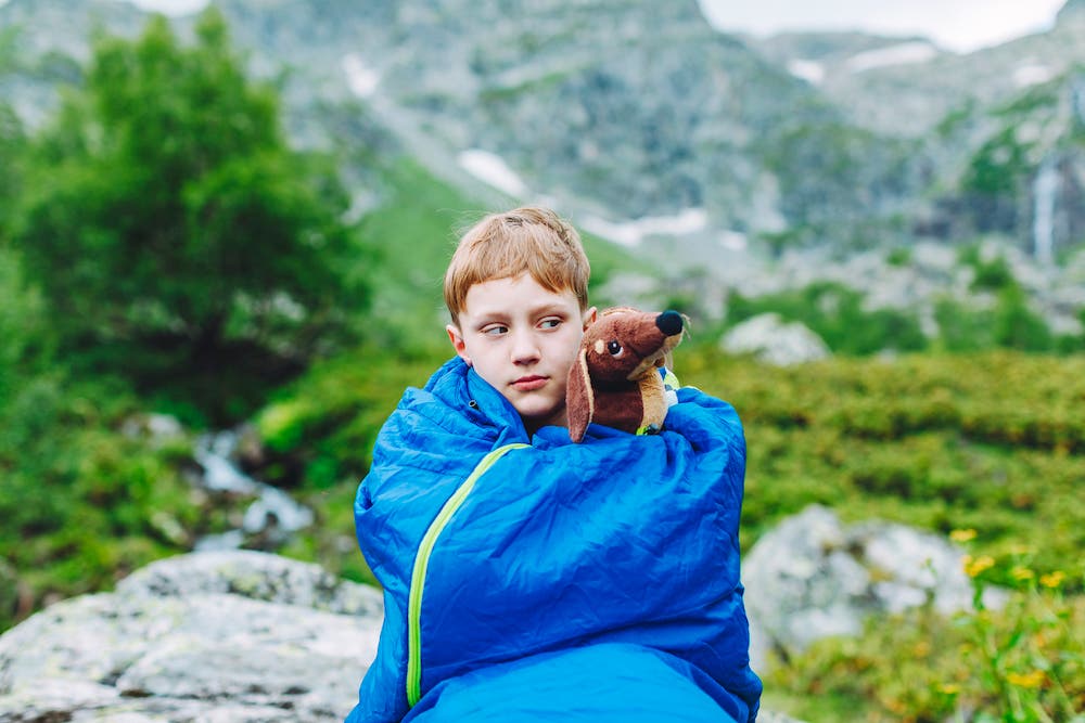 Un garçon dans son sac de couchage le matin, lors d’une randonnée en montagne