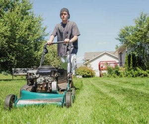 Adolescent portant des écouteurs et une casquette à l'envers en train de tondre la pelouse